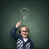 Schoolboy standing in front of a blackboard with a bright idea light bulb above his head concept for innovation, imagination and inspirational ideas