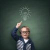 Schoolboy standing in front of a blackboard with a bright idea light bulb above his head concept for innovation, imagination and inspirational ideas