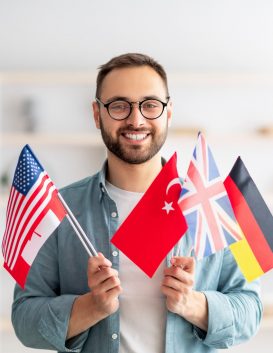 Handsome young guy holding bunch of diverse flags and smiling at camera indoors