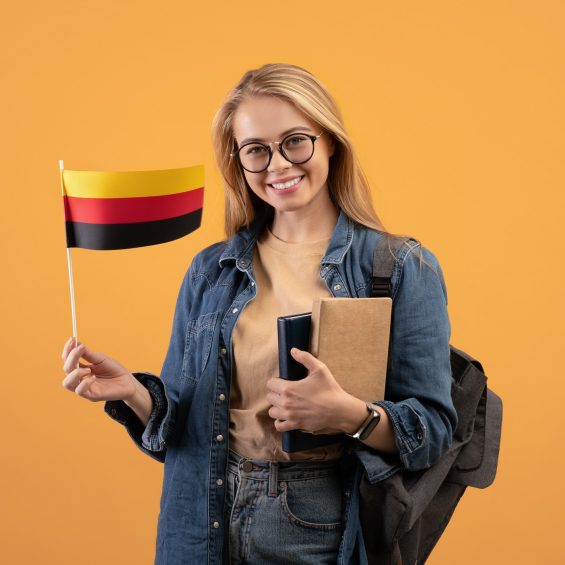 Happy young blonde lady student in casual with glasses, backpack and books holding small flag of