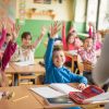 Large group of school children raising their hands ready to answer the question.