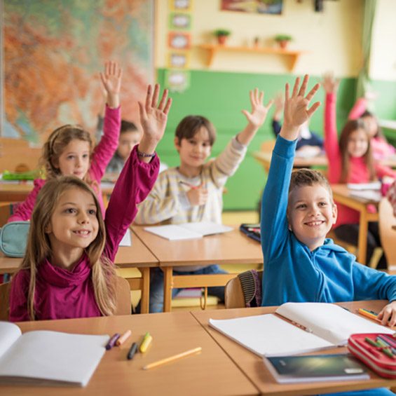 Large group of school children raising their hands ready to answer the question.